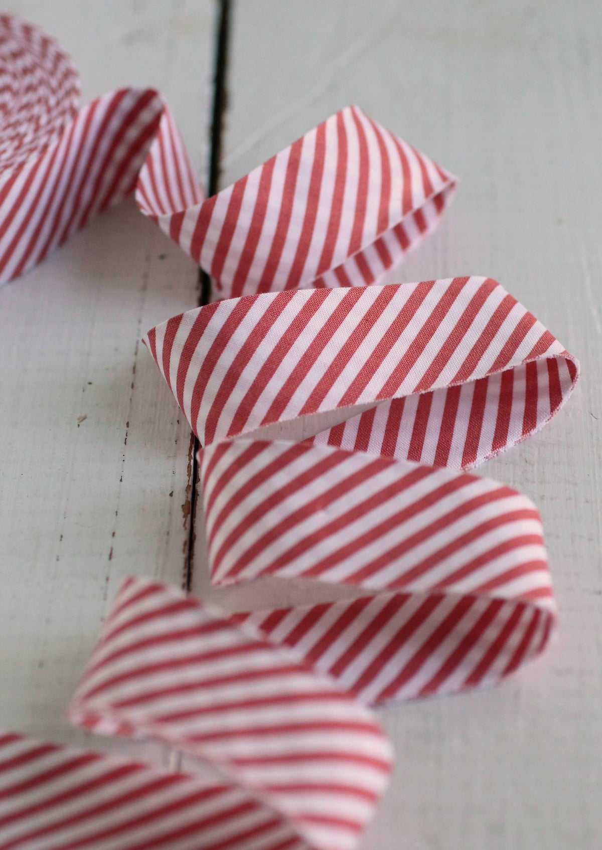 Red and white striped bias quilt binding arranged in loops on a light, distressed wooden surface.