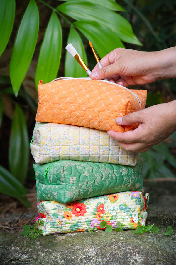 Stack of colorful fabric bags with a hand holding an orange one against a natural background