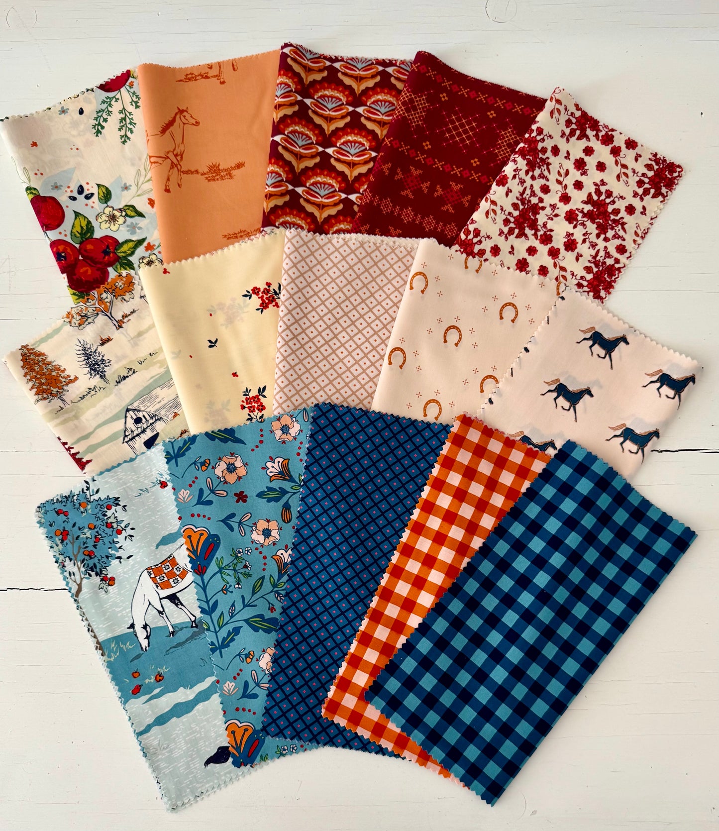 10" Squares of fabric on a white table. Horse themed fabrics.