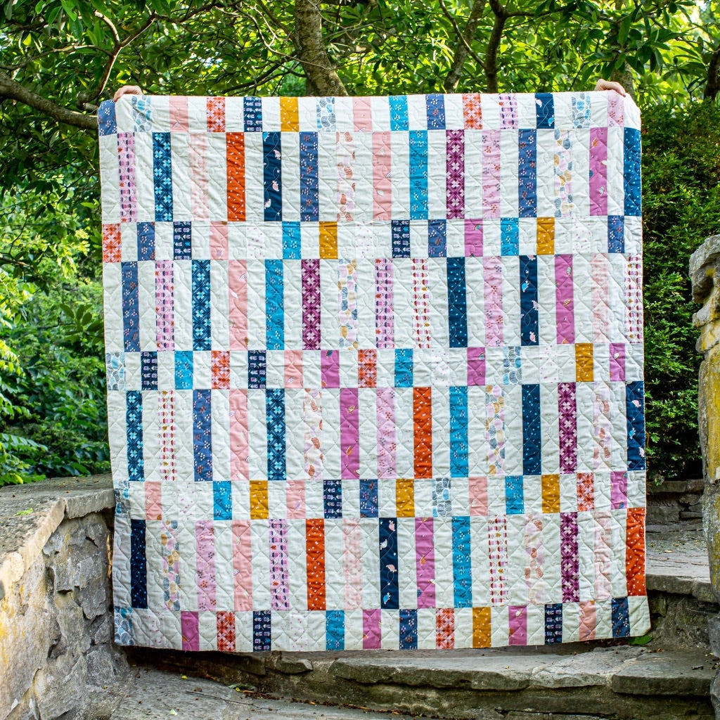 Colorful quilt with a geometric pattern held up outdoors against a natural background