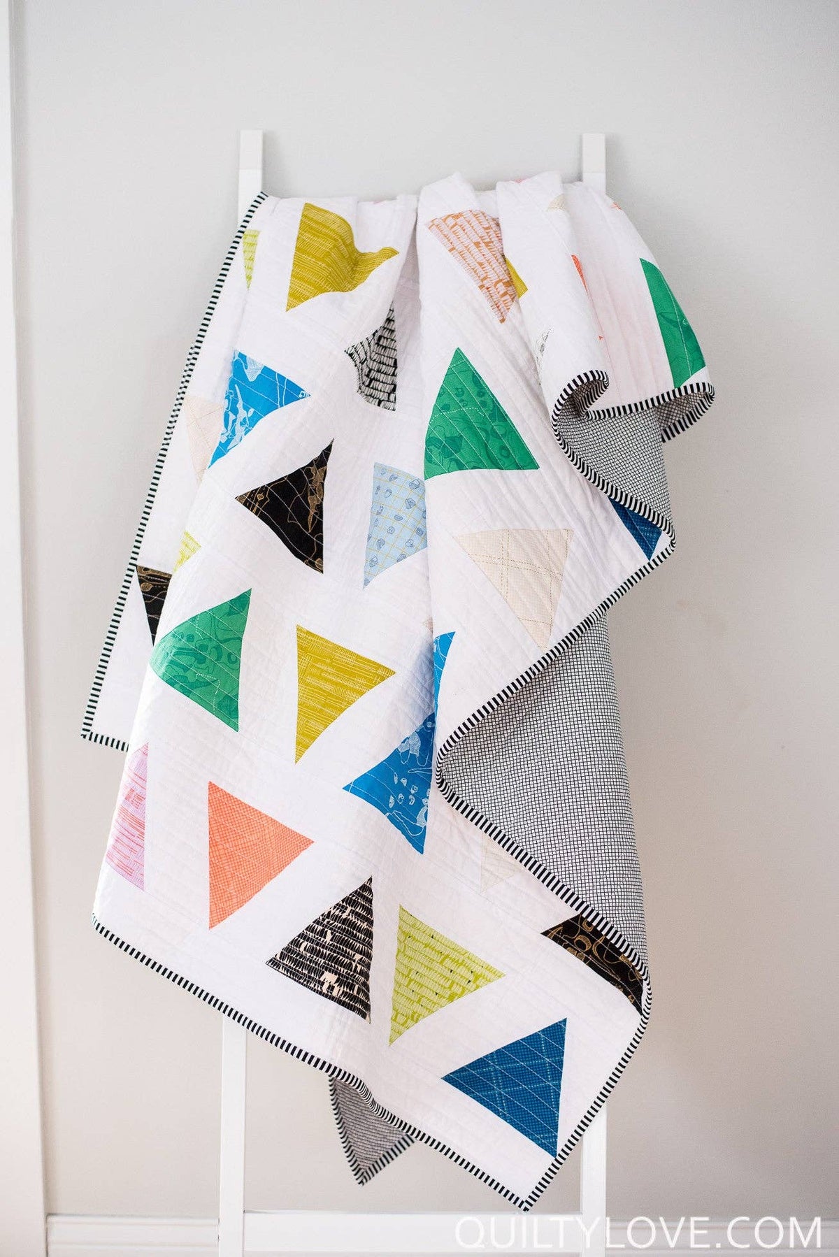 Colorful quilt with geometric patterns hanging on a rack against a white wall.