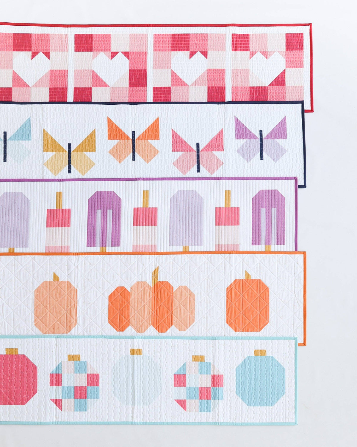 A close-up of a quilted fabric panel featuring a retro pattern of horizontal stripes with geometric shapes, including hearts, butterflies, popsicles, pumpkins, and ornaments in pink, orange, purple, and blue.
