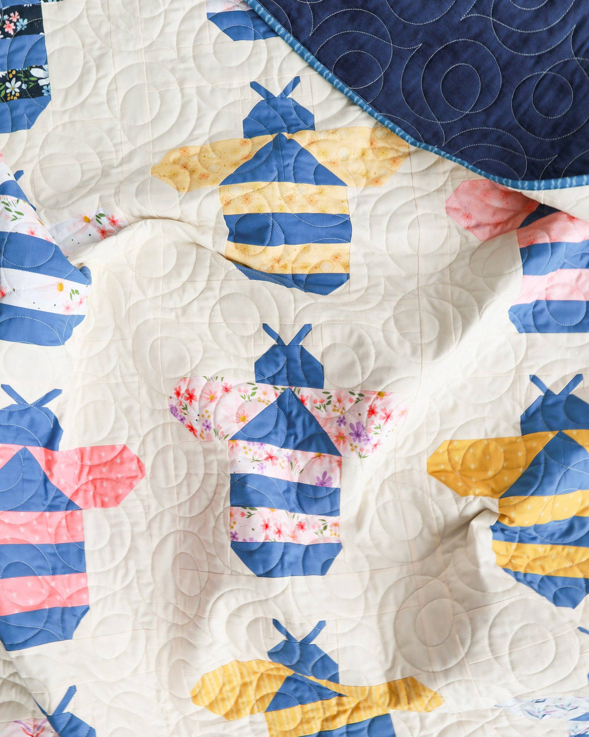Quilt with bee-themed design featuring blue, yellow, and pink colors on a white background.