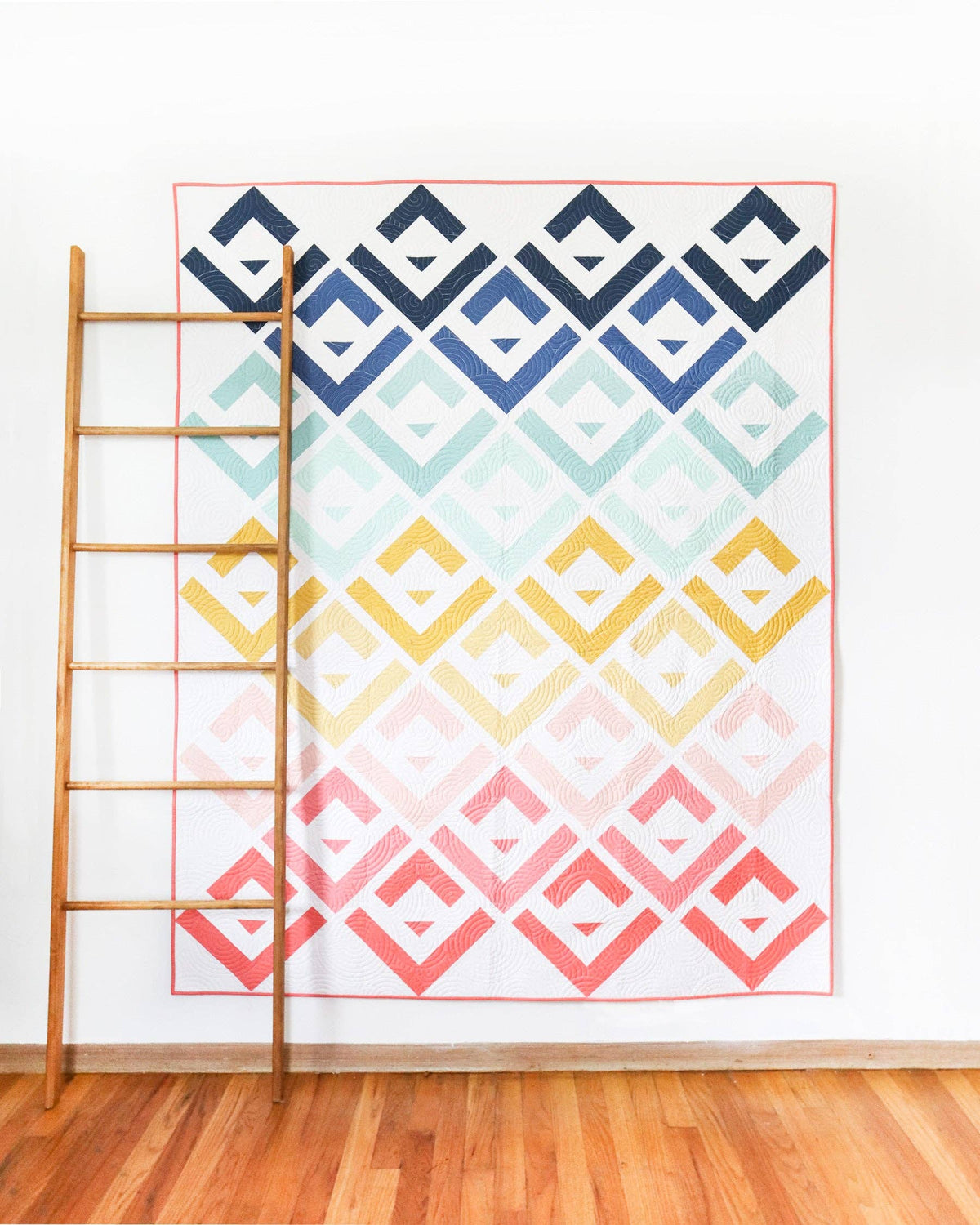 Colorful geometric patterned quilt on a wooden ladder against a white wall.