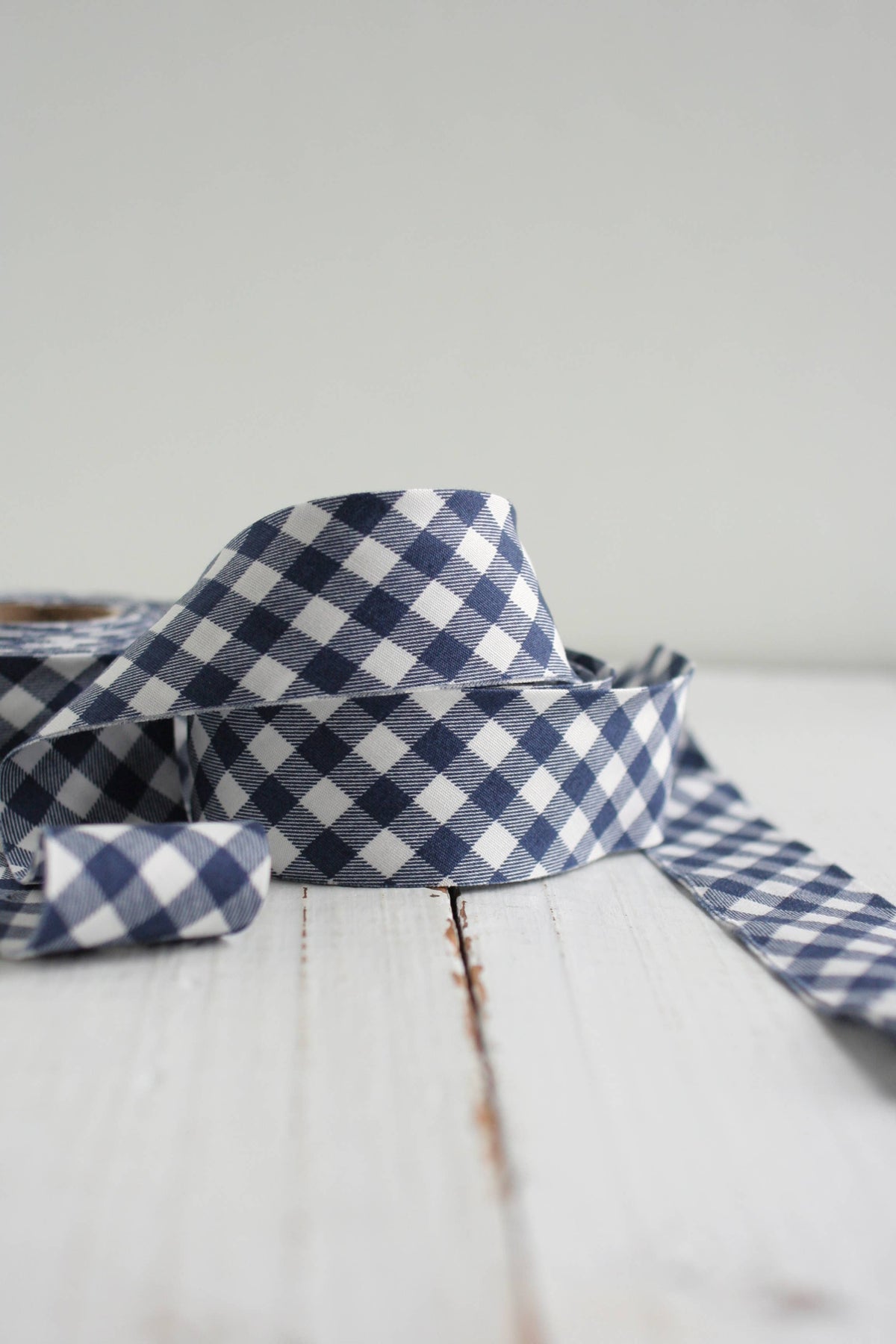 A close-up of a navy and white gingham bias quilt binding on a white wooden surface against a light gray background.