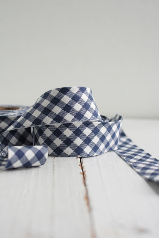 A close-up of a navy and white gingham bias quilt binding on a white wooden surface against a light gray background.