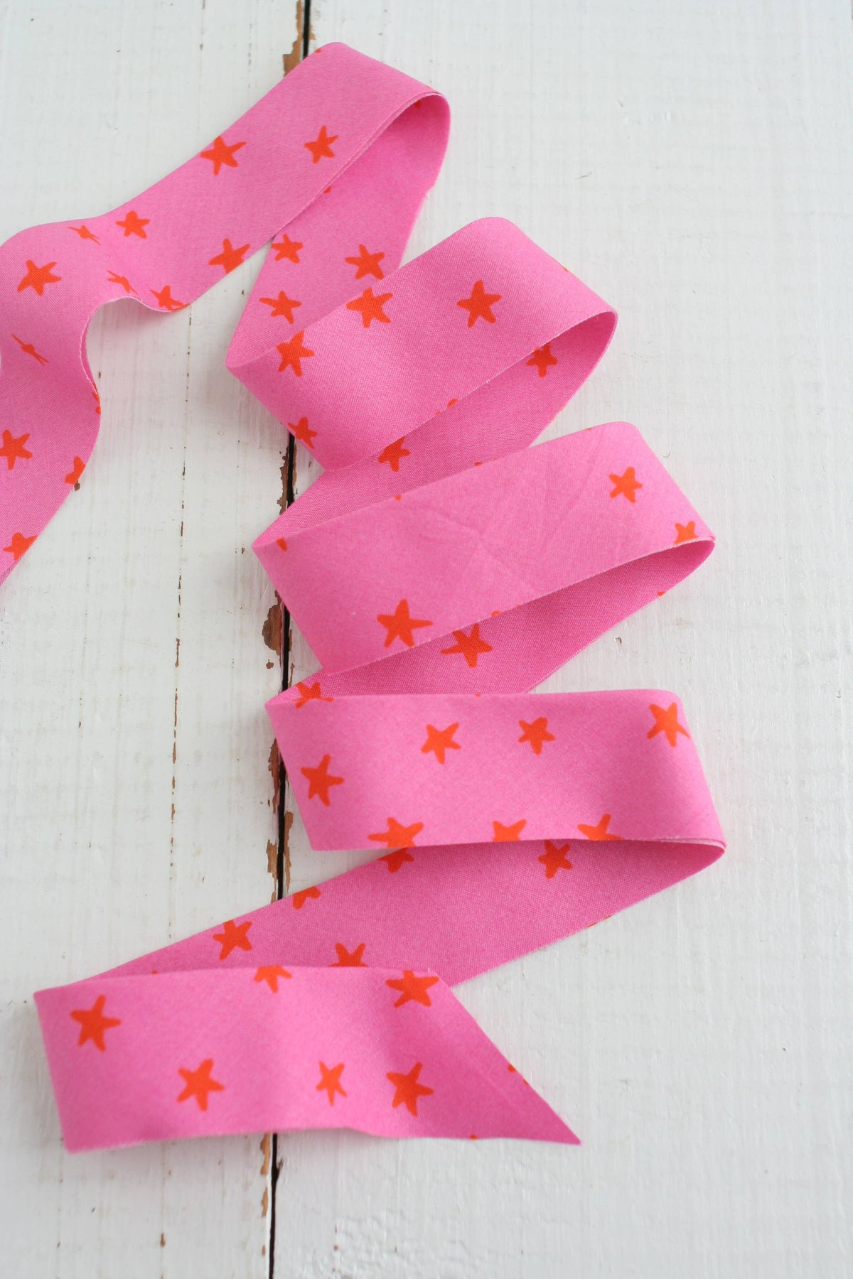 Pink ribbon with orange star patterns on a white wooden surface