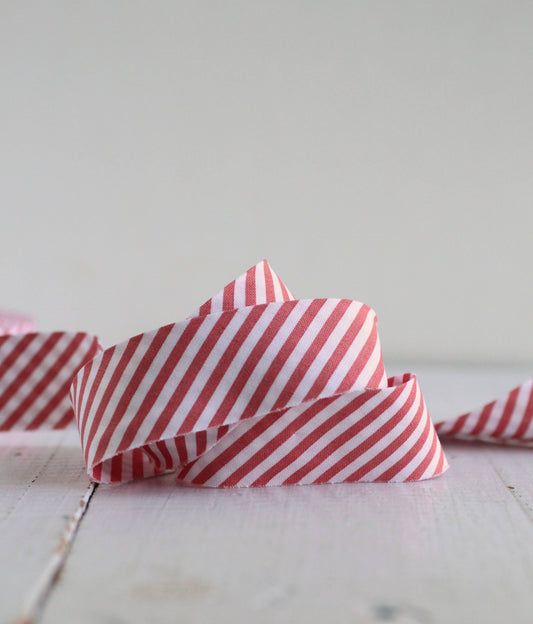 A close-up of a red and white striped bias quilt binding, styled like candy canes, coiled on a light-colored wooden surface against a soft, neutral background.