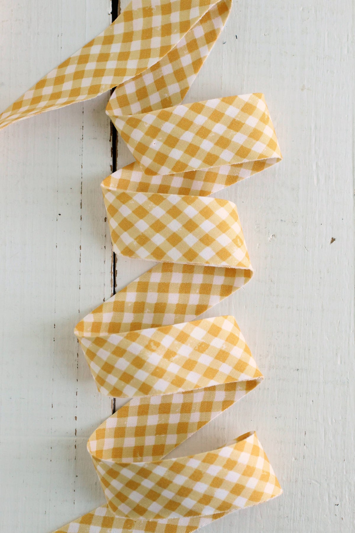 Yellow and white gingham quilt bias binding on a white painted wooden surface.
