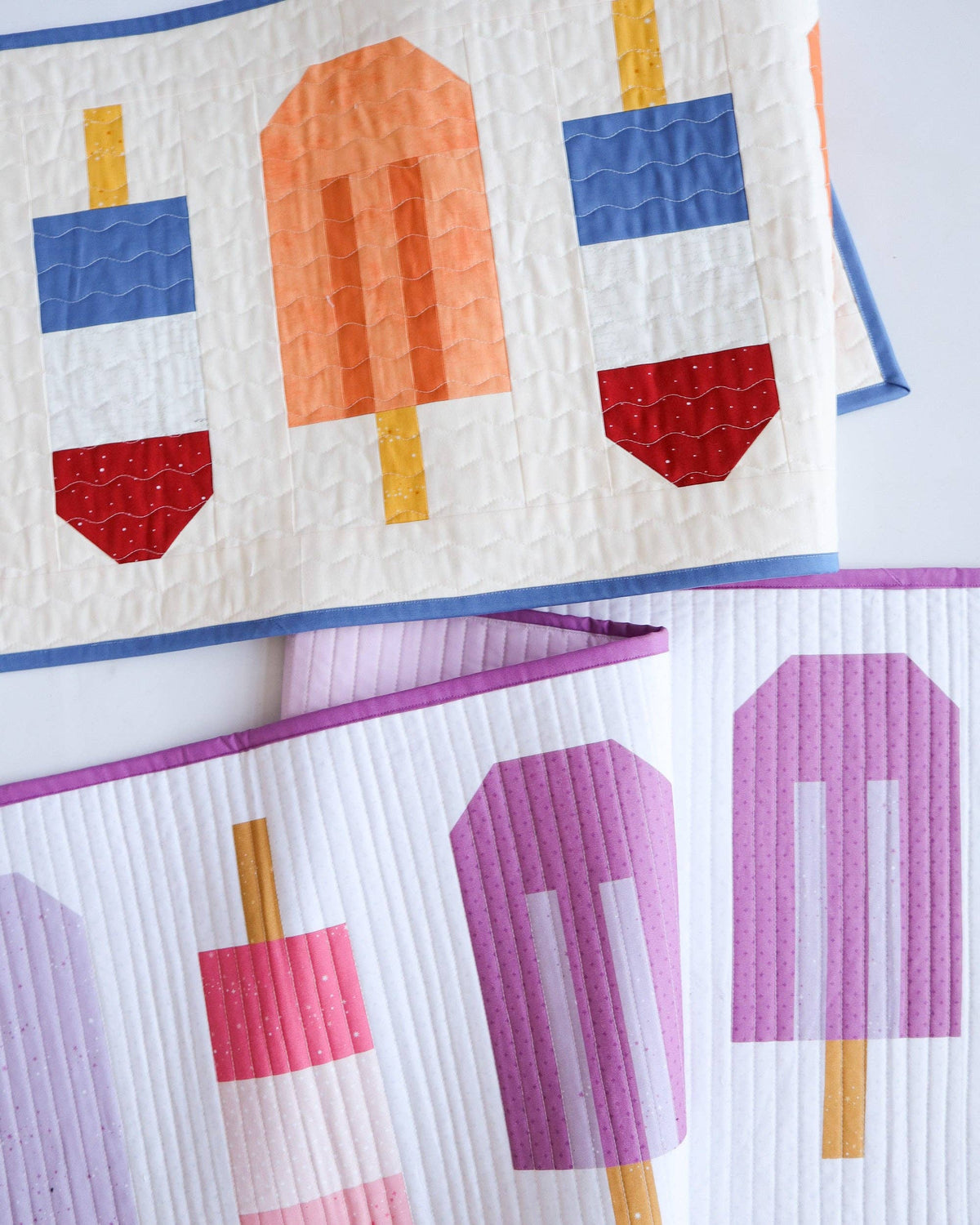 A close-up of a quilted textile featuring stylized popsicle designs in multiple colors, including blue, red, orange, pink, and purple on a white background.