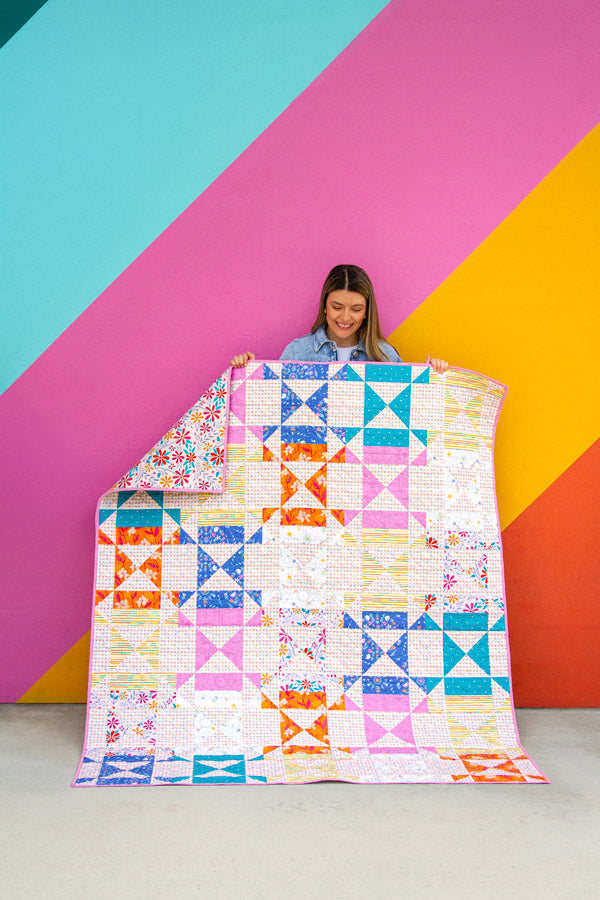 Person holding a colorful quilt against a multicolored geometric background