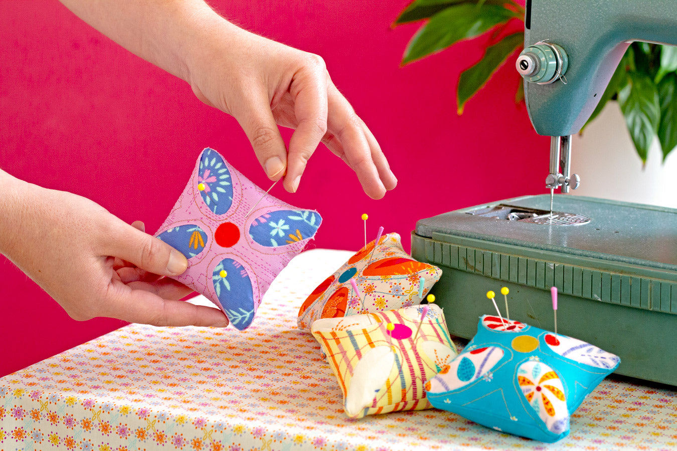 Handmade butterfly-shaped cushions with colorful patterns on a sewing machine and pink background