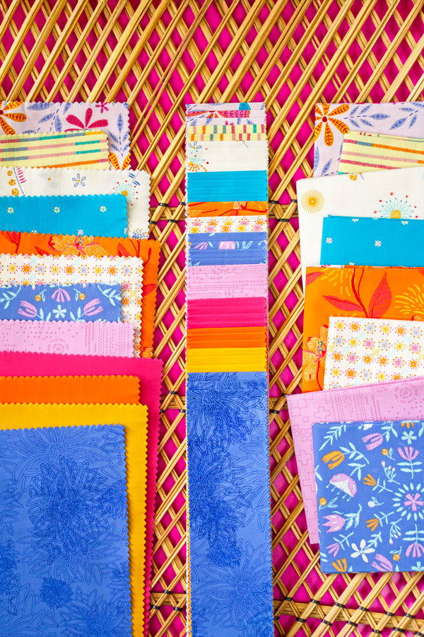 Colorful fabric swatches arranged in a pattern against a pink woven background