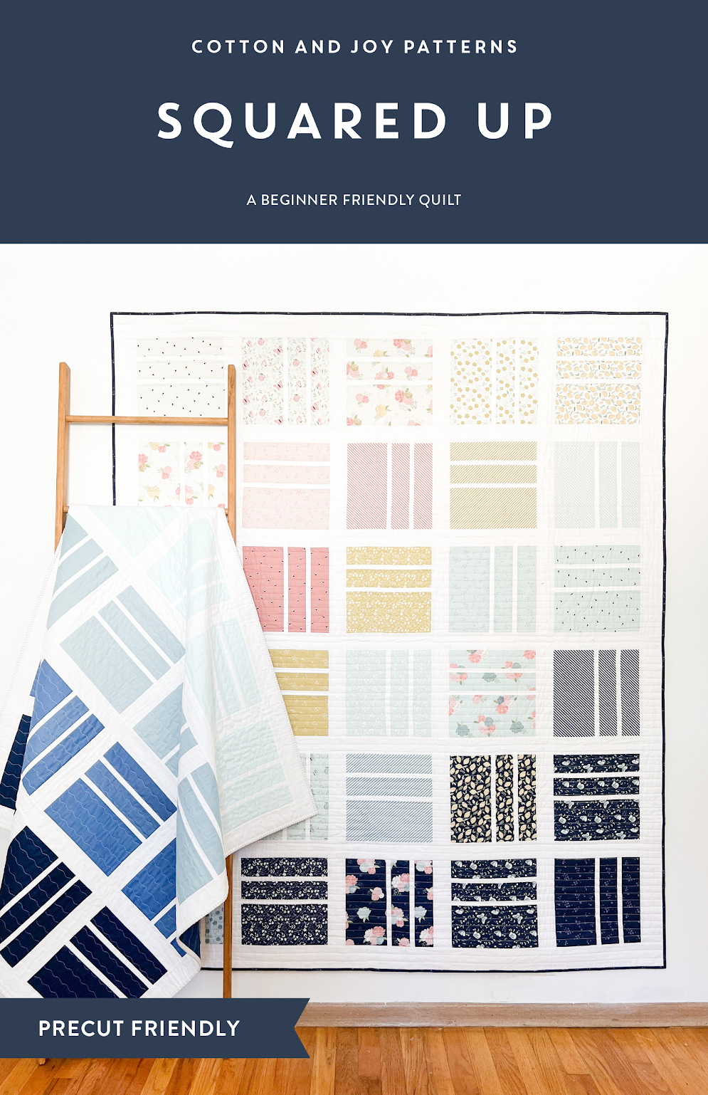 Quilt with various patterns hanging on a wall, accompanied by a folded fabric panel.