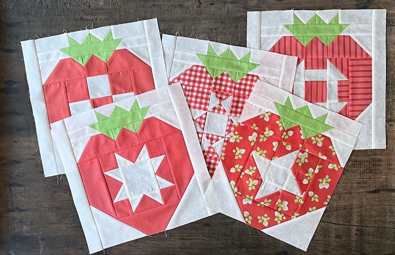 Set of strawberry-themed quilt blocks on a wooden surface