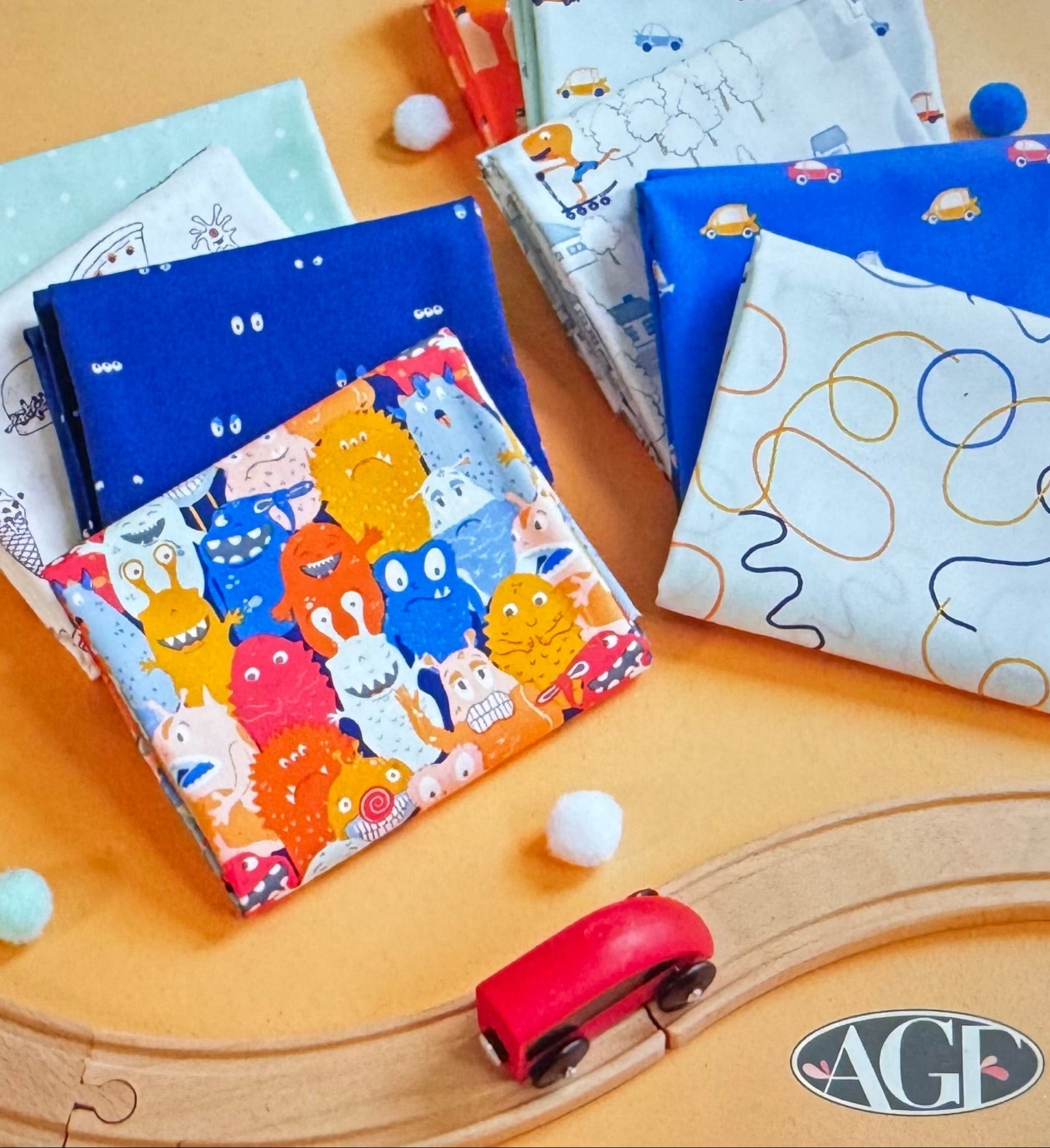 Collection of colorful fabric swatches with cartoon designs on a wooden surface, featuring the brand 'AGF Studio'.