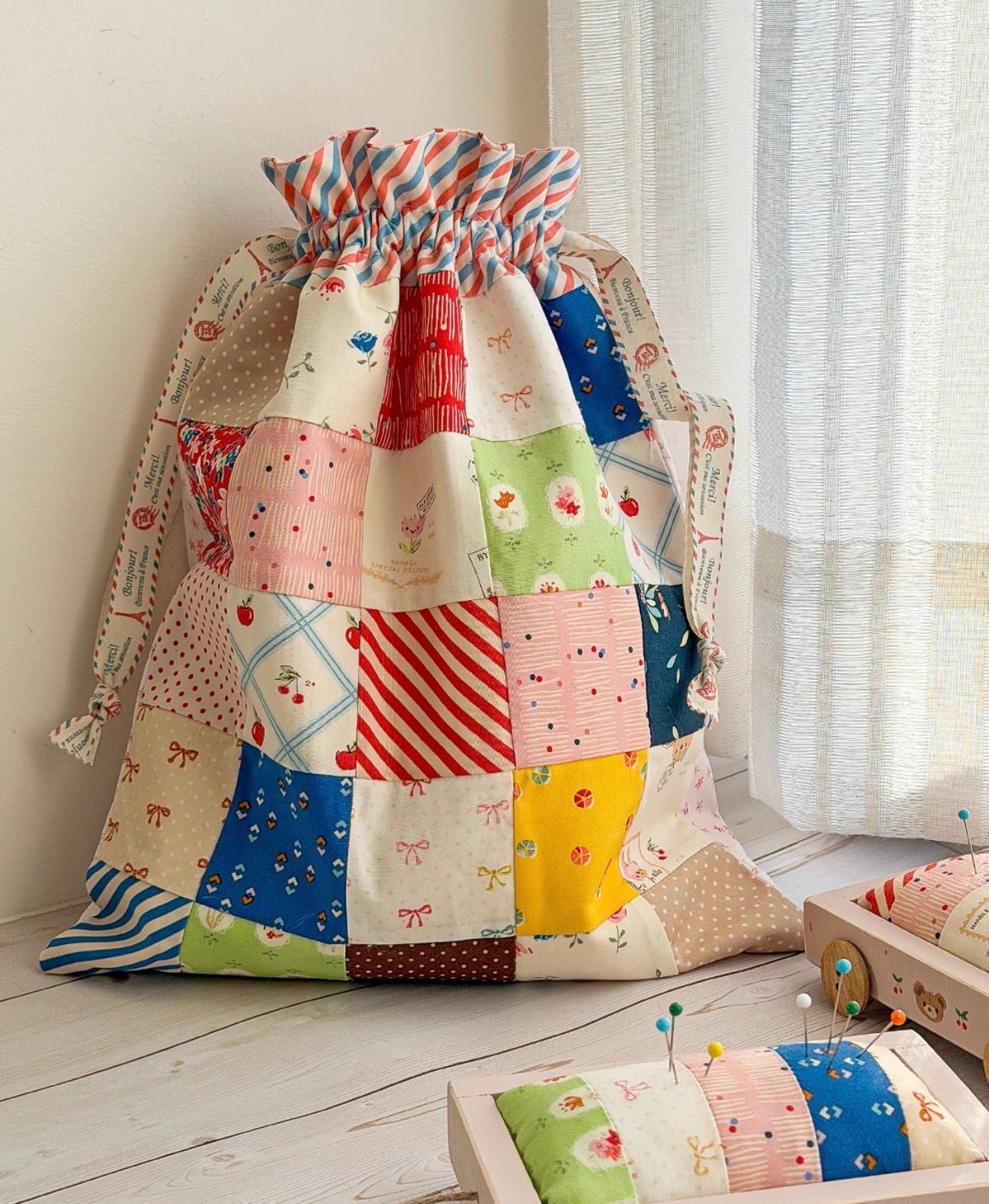 Colorful patchwork drawstring bag on a wooden floor with a curtain in the background