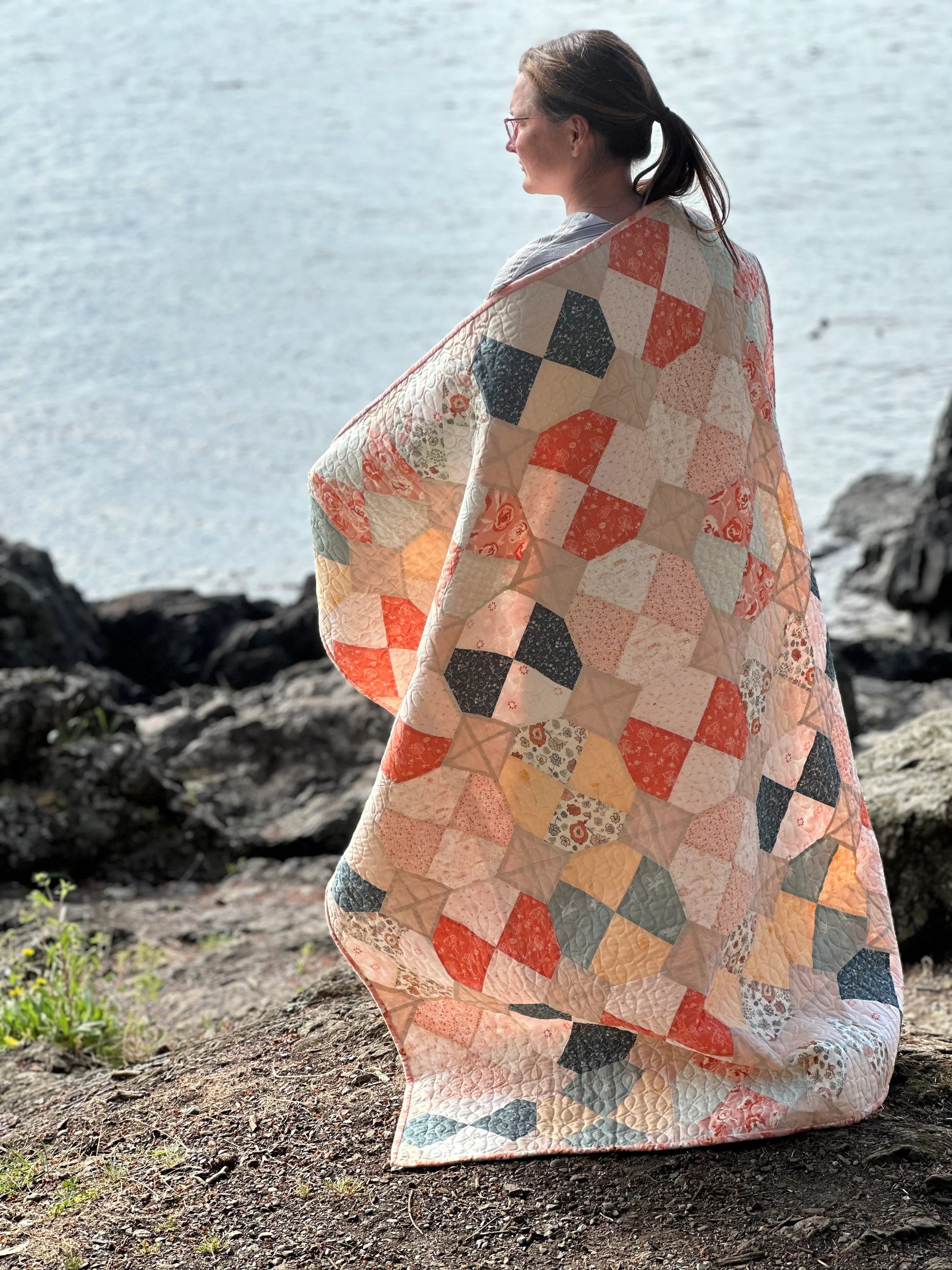 Girl on a beach wrapped in scrappy quilt.