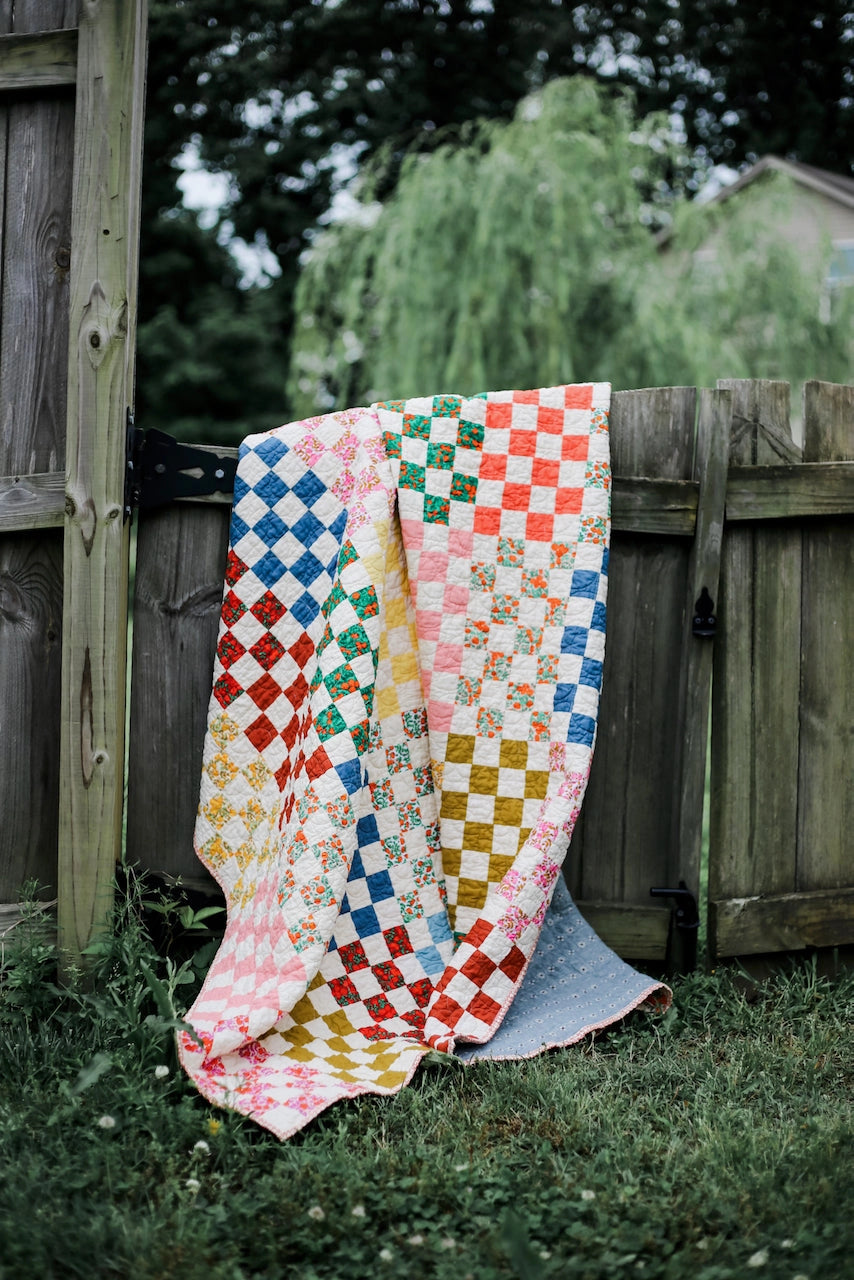 Colorful quilt draped over a wooden gate with a garden background