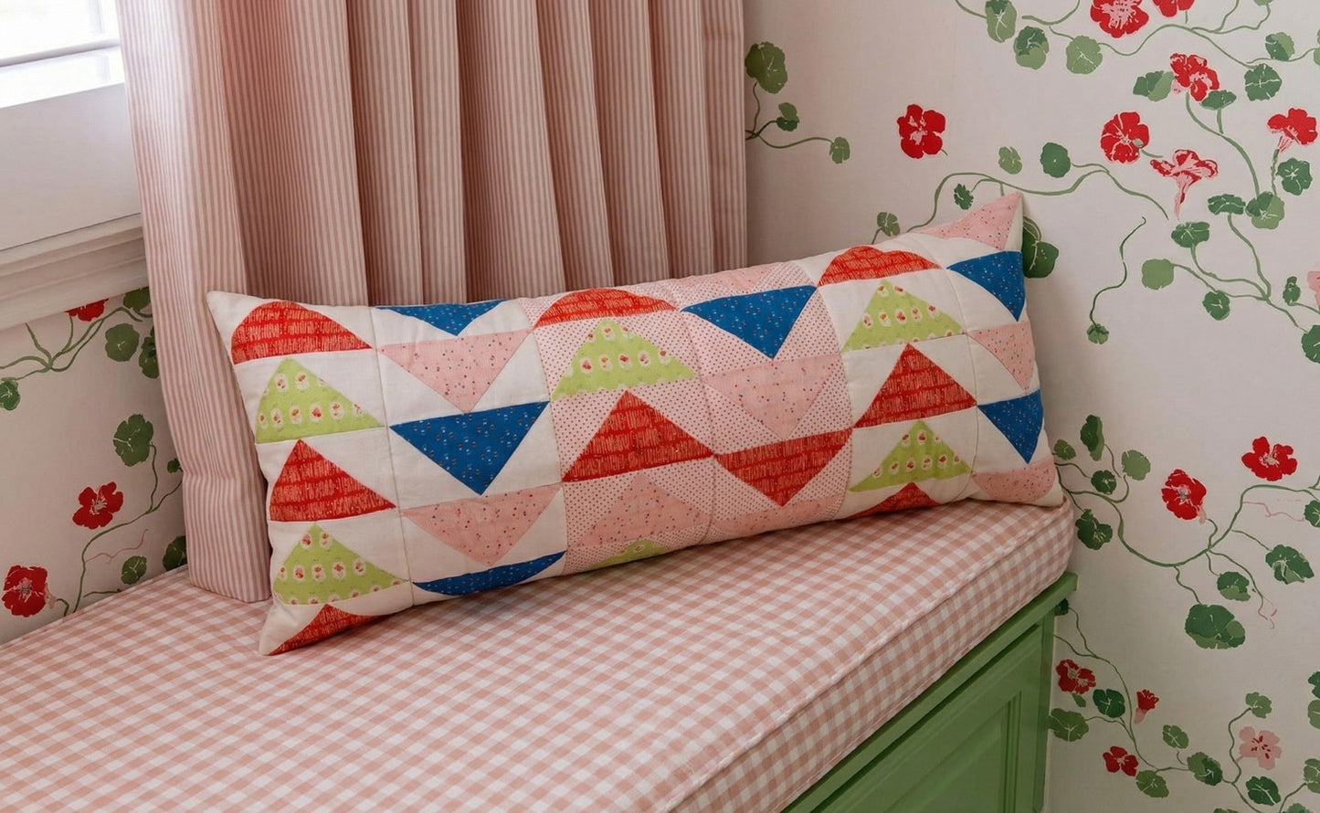 Decorative pillow with geometric pattern on a cushioned bench against floral wallpaper.