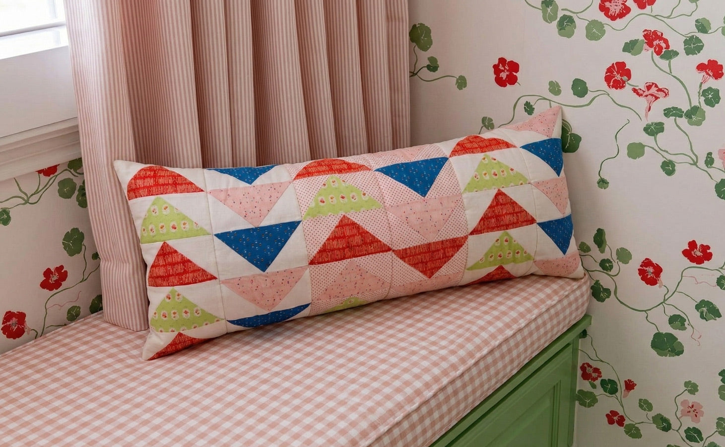 Decorative pillow with geometric pattern on a cushioned bench against floral wallpaper.