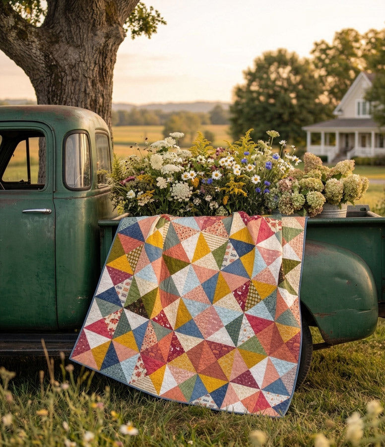 Colorful quilt on a vintage truck bed with flowers and a house in the background