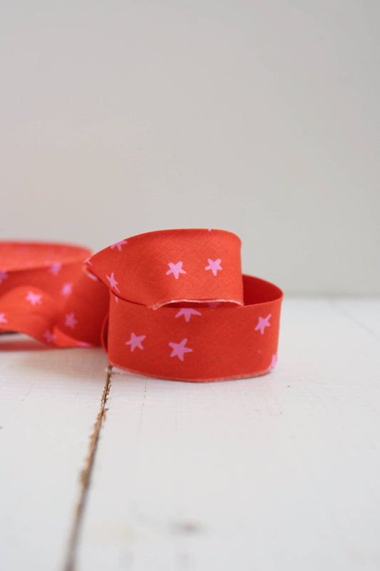 Red bias quilt binding with pink stars on a white surface