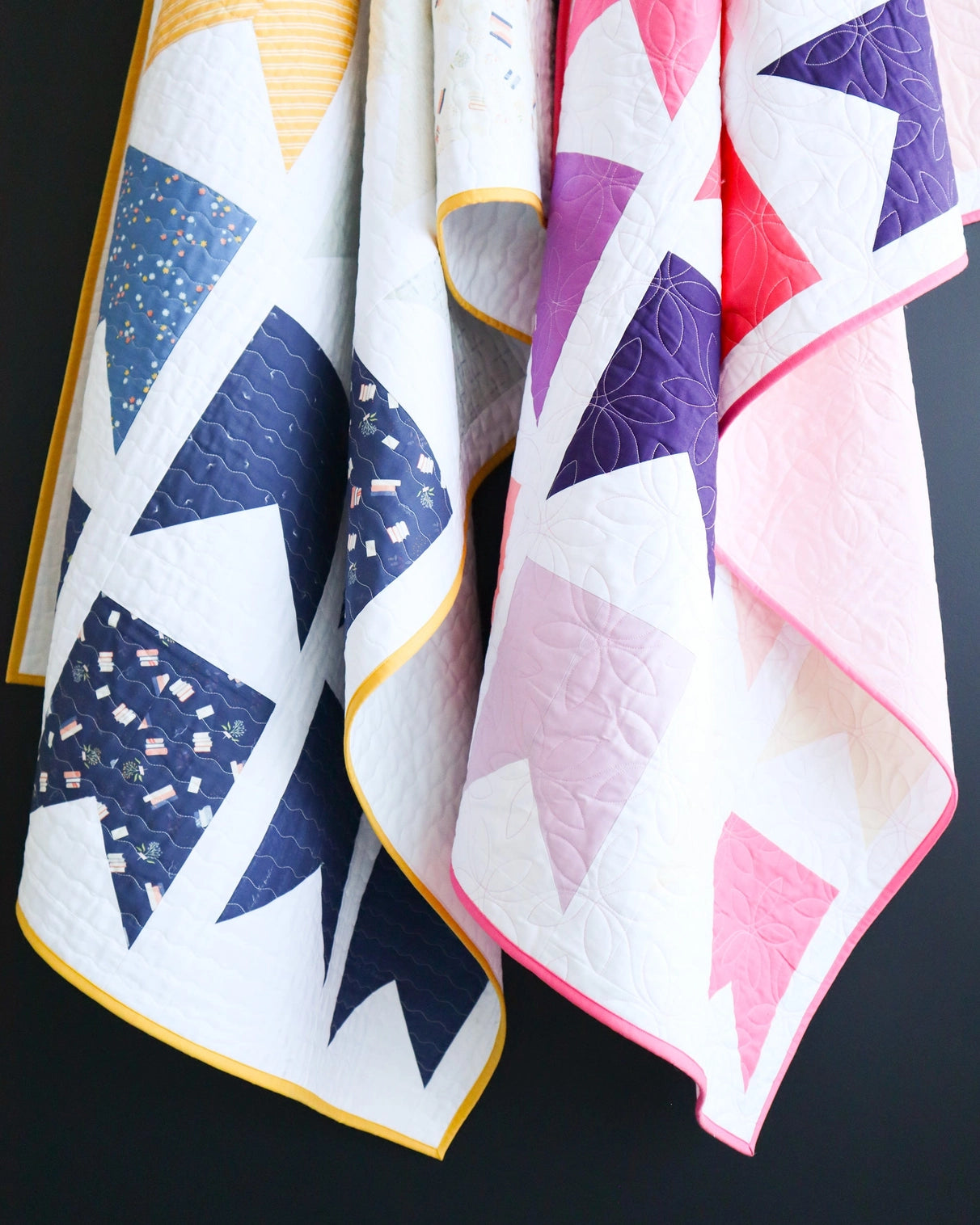 Two geometric-patterned quilts with colorful borders on a dark background