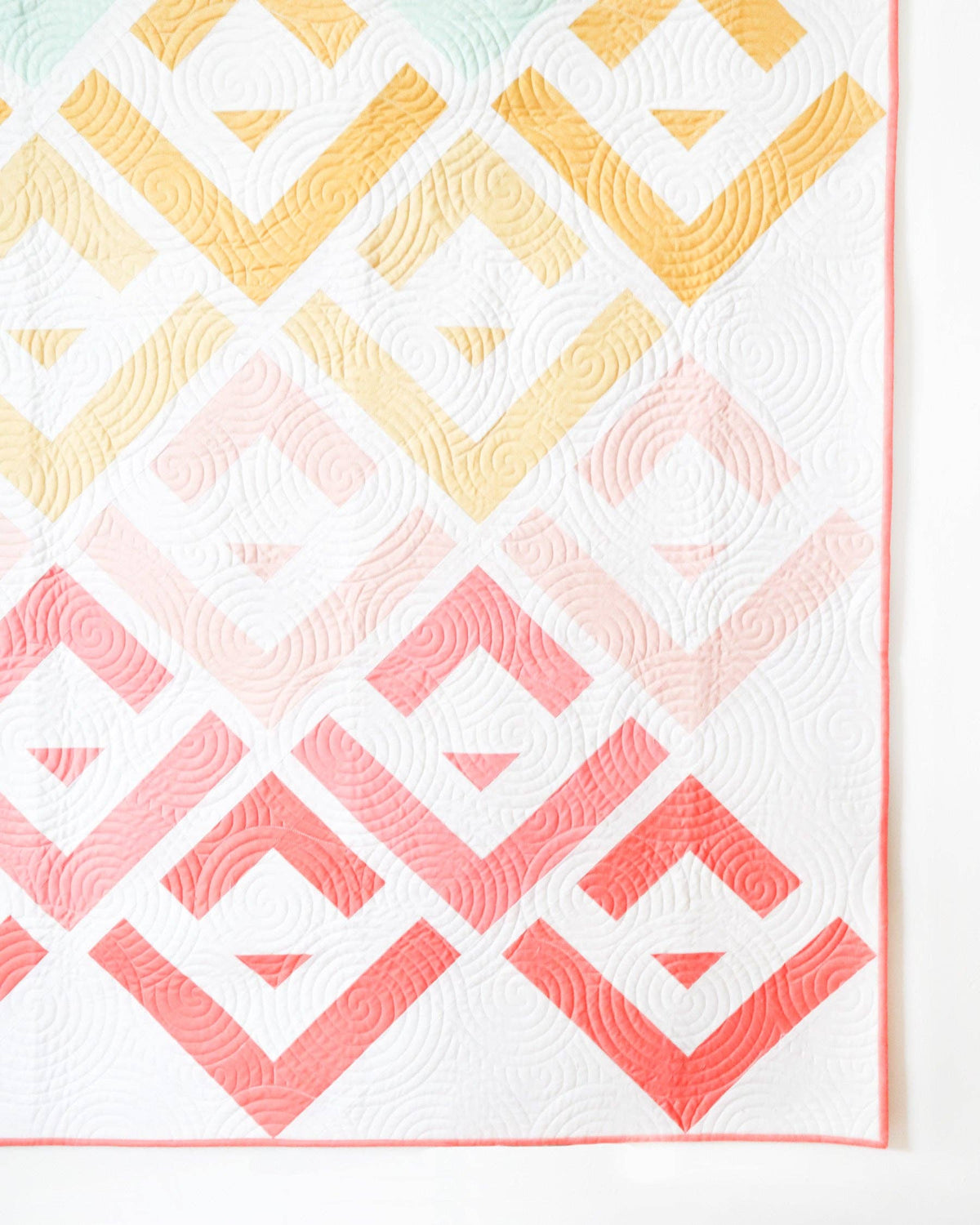 Quilt with geometric pattern in pink, yellow, and white on a white background