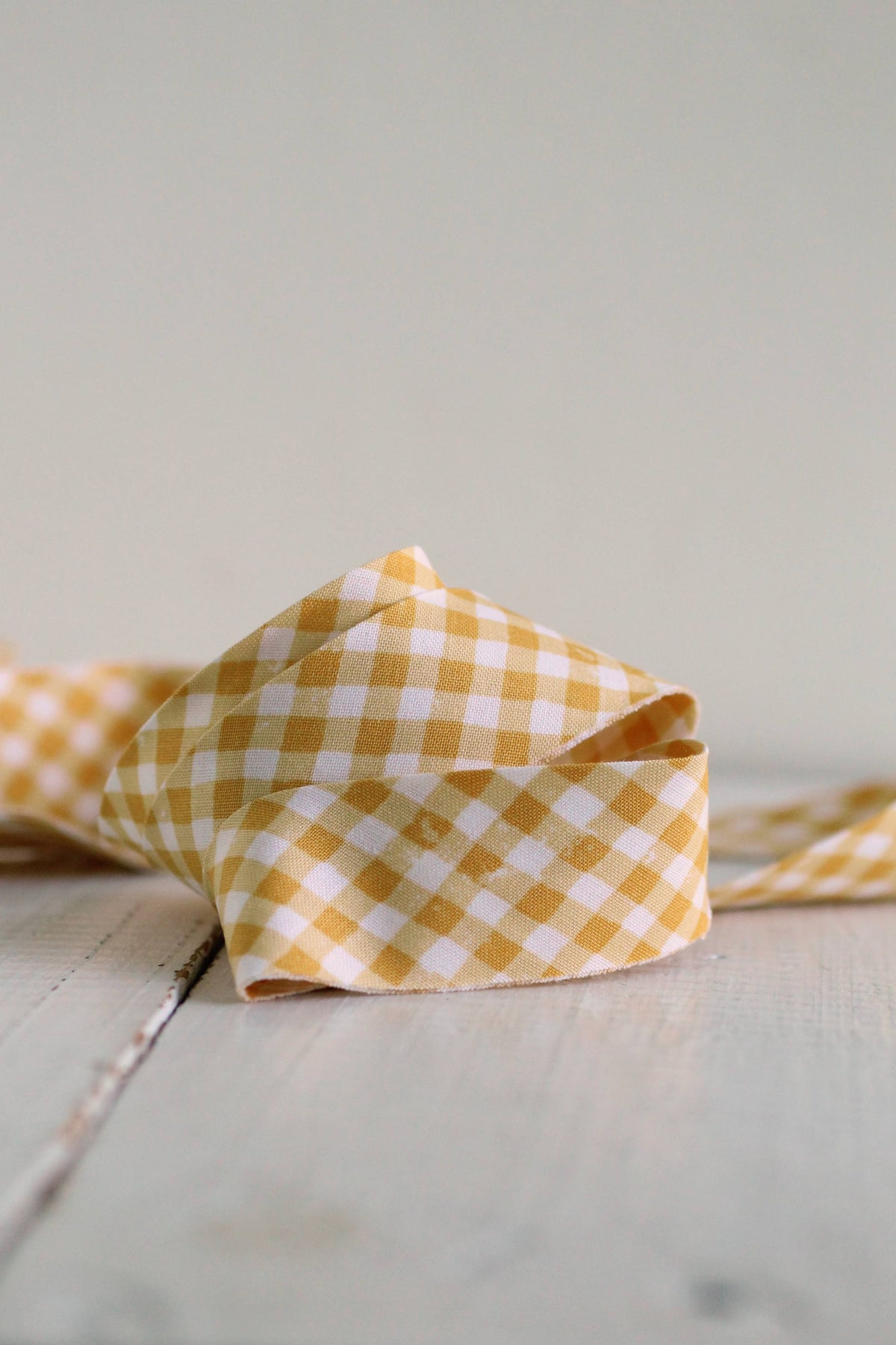 A folded yellow and white gingham check bias quilt binding on a light gray surface with a soft gray background.