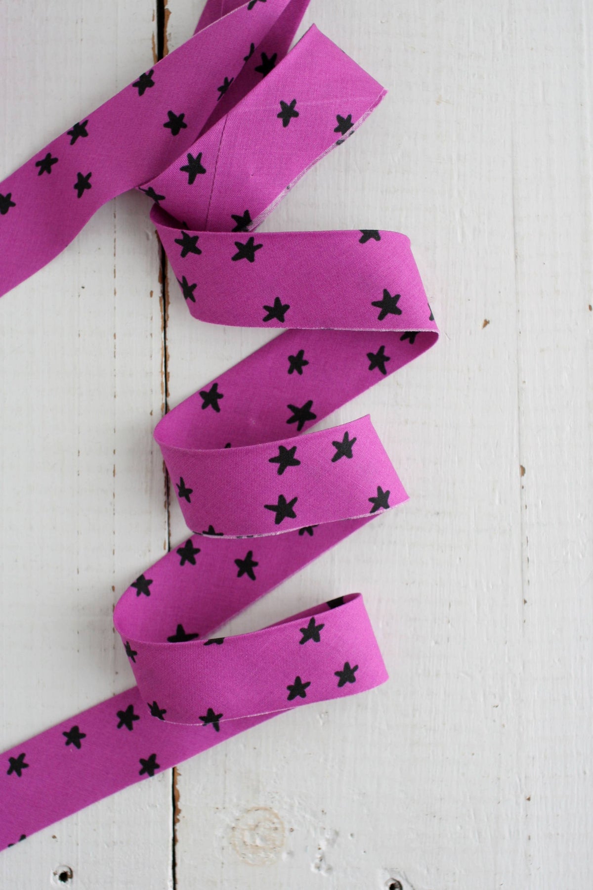 Purple bias quilt binding with black star patterns on a white wooden surface