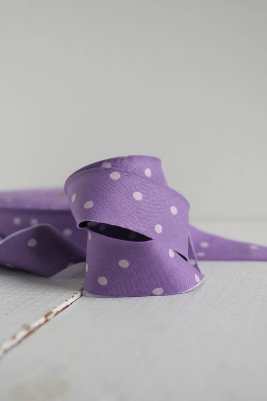 Purple ribbon with white polka dots on a light gray background