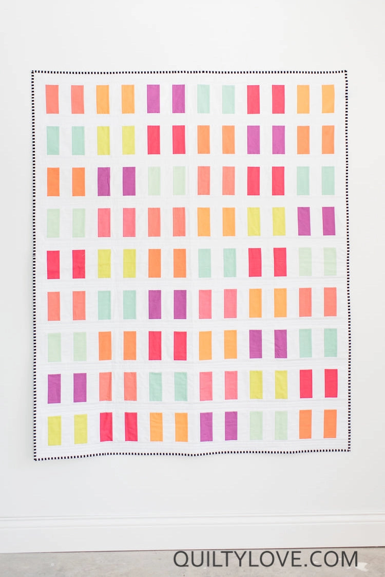 Colorful quilt with geometric pattern on a white background, featuring the brand 'Quilty Love'.