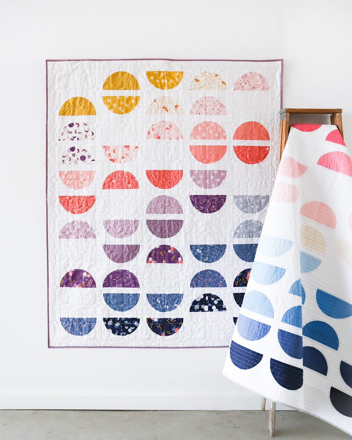 Colorful geometric patterned quilt on a wooden hanger against a white wall.