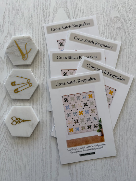 Cross Stitch Keepsakes pattern books with decorative pins on a light wooden surface