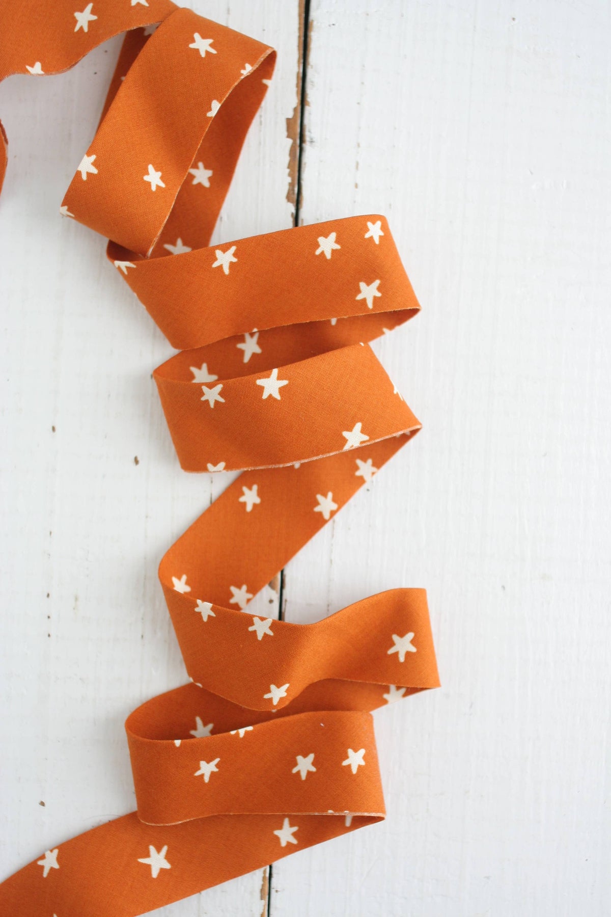 Orange quilt binding tape with white star patterns on a white wooden background