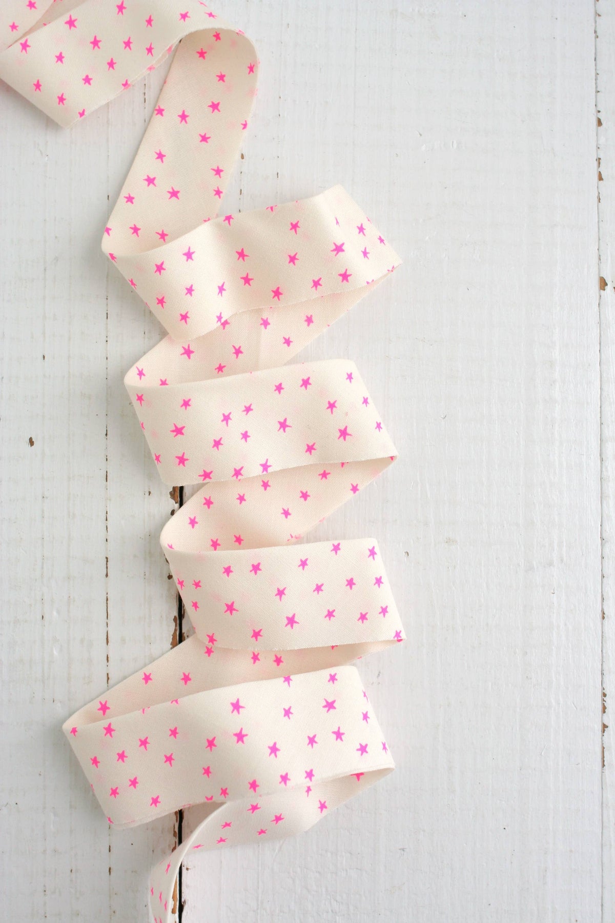 Off-white with pink star patterned bias quilt binding on a white wooden background