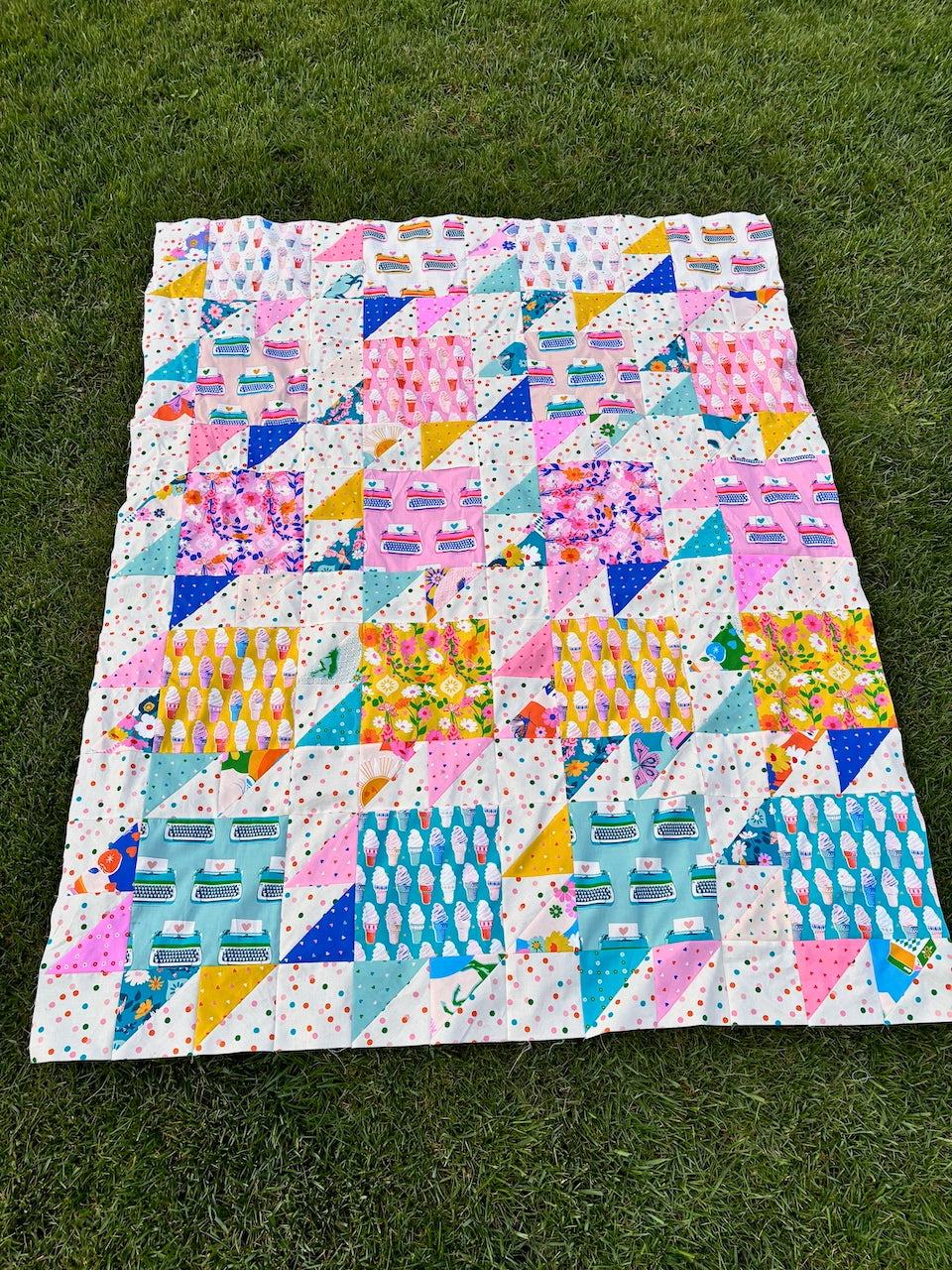 Colorful quilt with geometric patterns on a grassy background