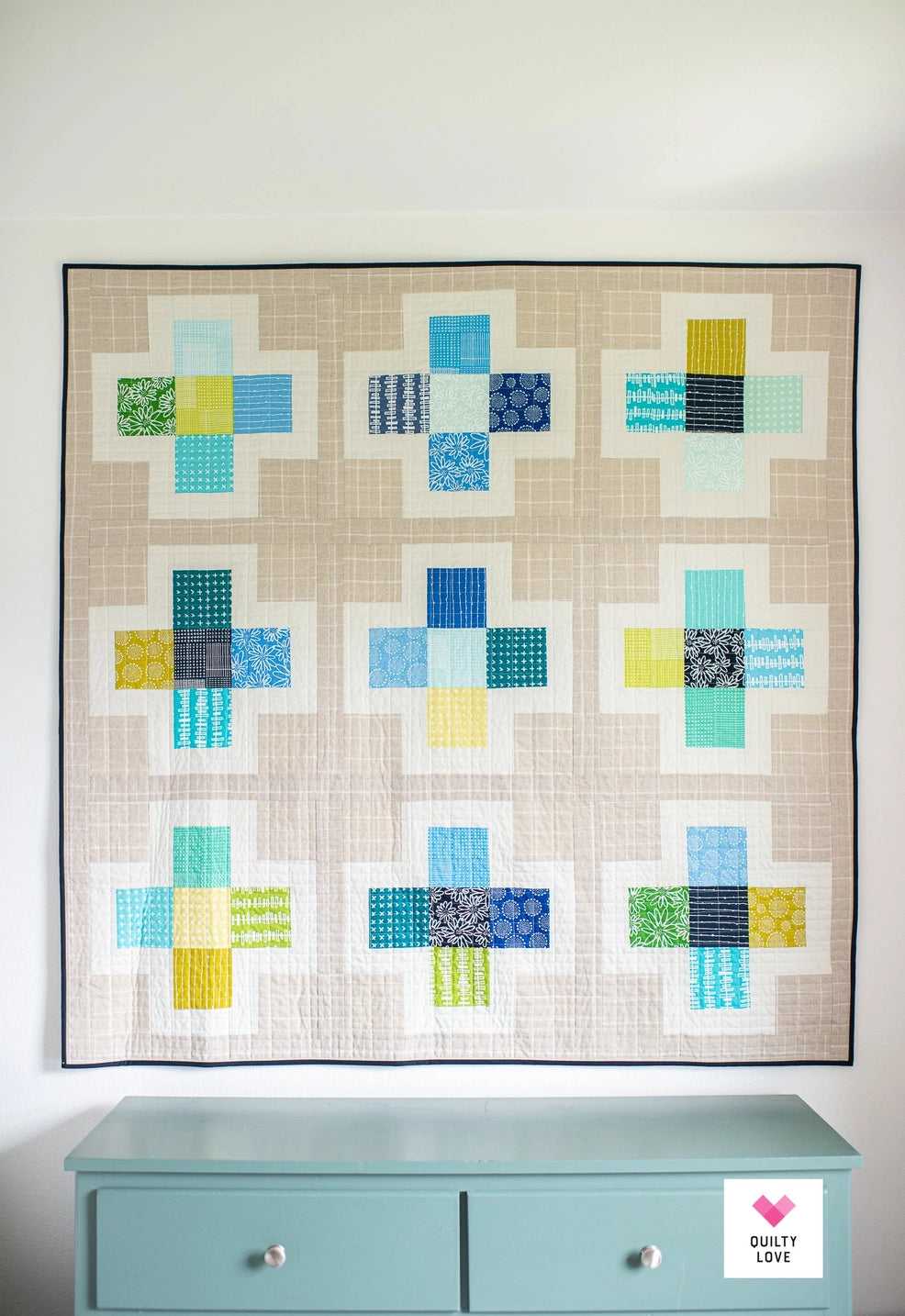 Quilt with geometric pattern on a light blue dresser against a white wall
