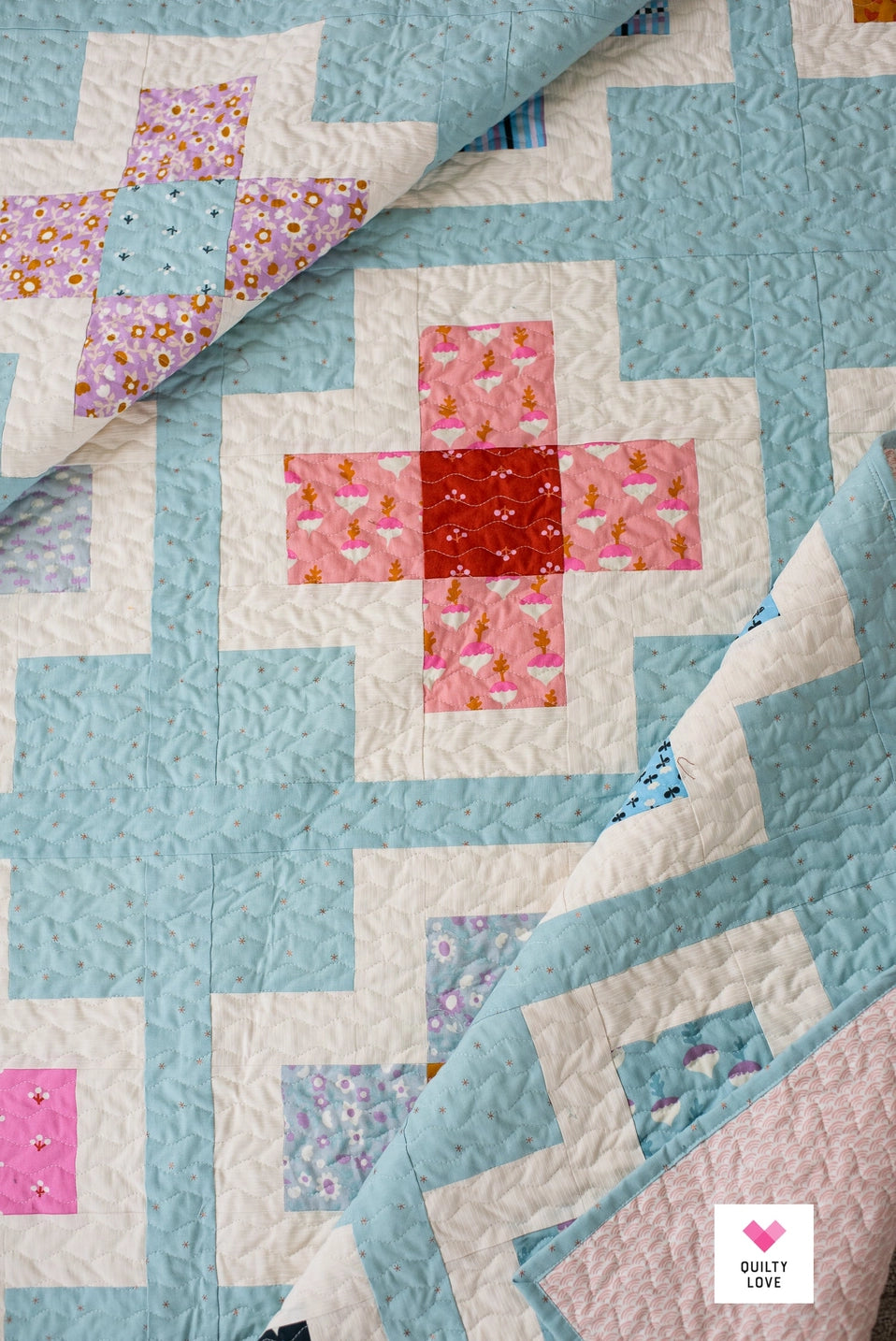 Quilt with geometric pattern featuring pink, red, and blue colors on a light blue background.